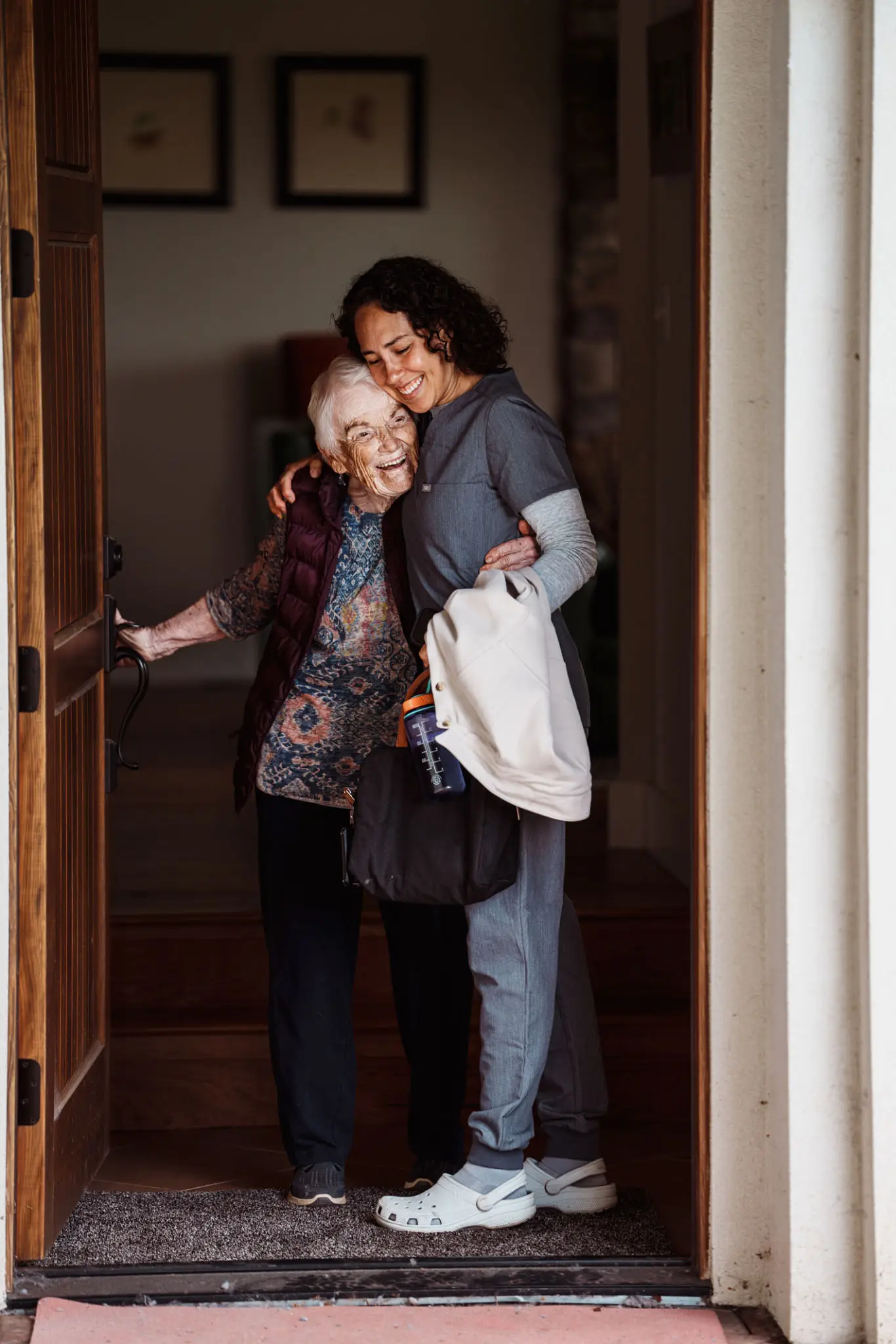 Caregiver hugging elderly woman at doorway