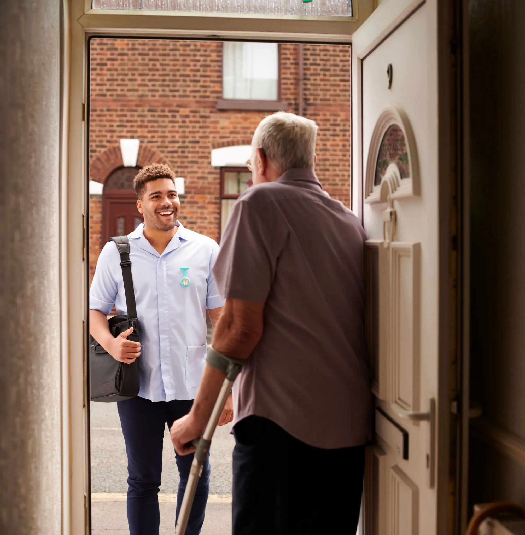 Caregiver greeting elderly man at front door